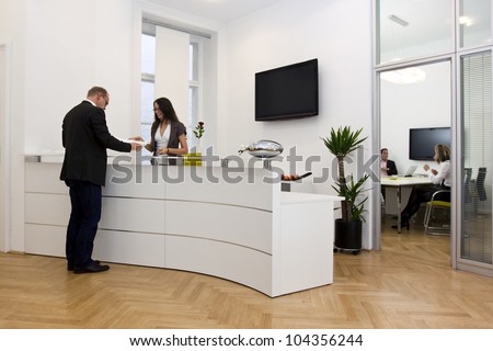 A front desk lady doing her job very well and cheerfully while she's consulting a customer. The black space on the TV-screen could be used for any logos, some label signs or any graphic additions.