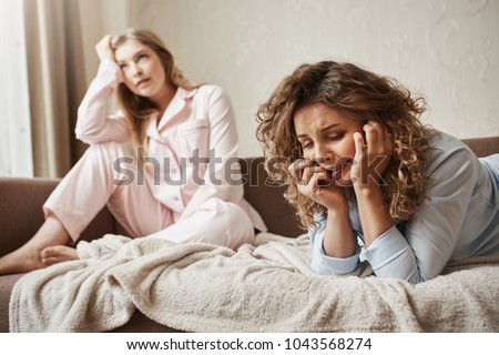 Girl cannot handle pressure, feeling miserable and sad. Gloomy crying woman lying in nightwear on sofa, whining and complaining on life while girlfriend is feeling bothered with dumb conversation Royalty-Free Stock Photo #1043568274
