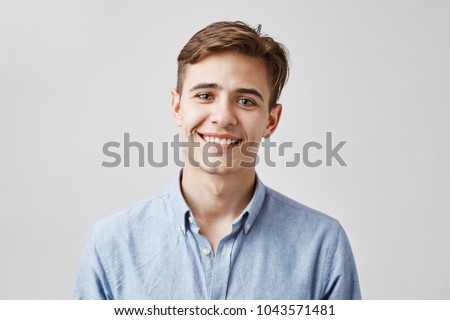 Cute boy with brown hair and beautiful smile standing next to the wall. His birthday is today so coworkers made surprise party. Guy looks happy he did not expected they will remember.