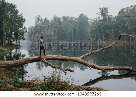 Traveller photographer standing on big tree and do pictures of tropical lake landscape