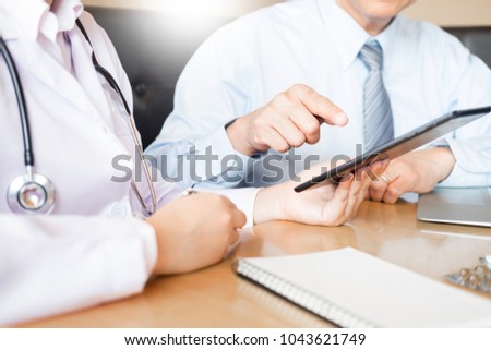 Two doctors discussing patient notes in an office pointing to tablet as they make a diagnosis or decide on treatment. Royalty-Free Stock Photo #1043621749