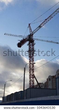 Tall red color metal tower cranes are working. Column cranes have high height. Blue sky woth white clouds are on a background.