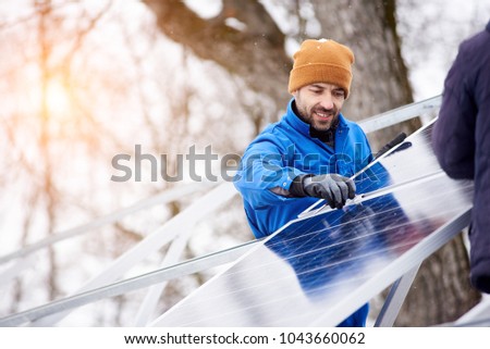 Handsome bearded mature male electrician worker smiling while installing solar pannels on power plant factory copyspace occupation working professionalism confidence job profession environment energy. Royalty-Free Stock Photo #1043660062
