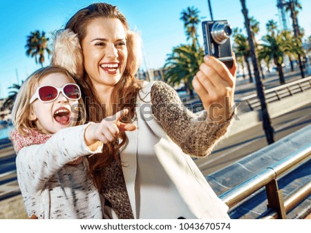 in Barcelona for a perfect winter. happy modern mother and daughter tourists on embankment in Barcelona, Spain pointing on something and taking photo with digital camera
