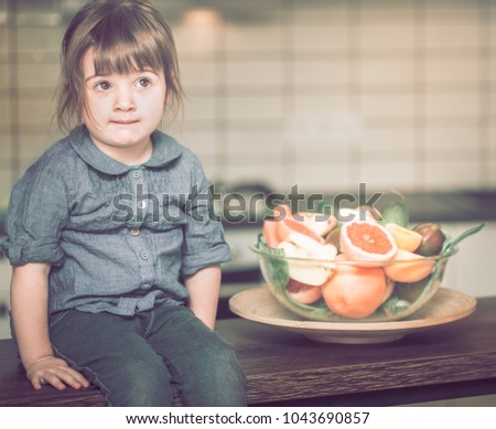 little cute thoughtful girl sitting near a plate with fruit on a kitchen table, concept of a healthy baby food