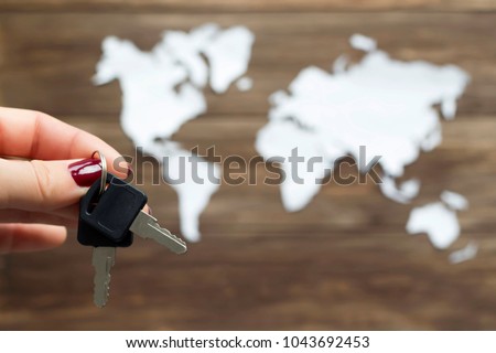 Hand holding keys and world map cutted from white paper on the wooden background. Management, security, discovery concept. Close-up, soft focus, copy space, mock up
