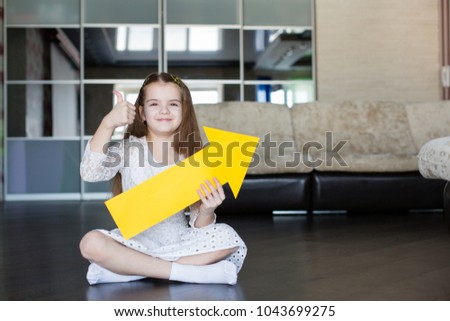 little cute caucasian girl in white dress holds a yellow arrow in hands