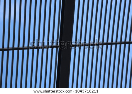 Close up view from bellow of a modern ceiling building made of metallic railing bars. Pattern of dark parallel lines with a blue sky in background. Abstract architectural image. Striped composition. 
