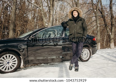 Man looking excited standing in front of his newly bought car in winter forest road. Auto business. Winter car service