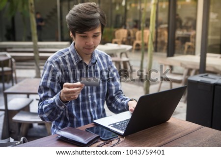 Southeast Asian handsome man in shirt using smartphone at cafe while holding credit card in the hands, on-line shopping outdoors