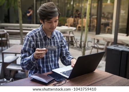 Southeast Asian handsome man in shirt using smartphone at cafe while holding credit card in the hands, on-line shopping outdoors