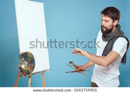  painter with a paintbrush stands at the easel on a blue background, palette, art                              