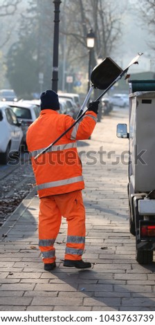sweeper with an orange jacket collecting rubbish along the streets of a big city