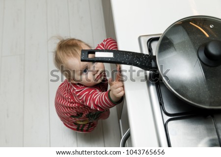child safety at home concept - toddler reaching for pan on the stove in kitchen Royalty-Free Stock Photo #1043765656