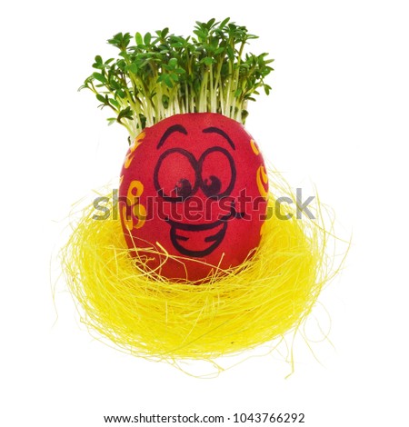 Easter egg painted in a funny smiley face and colorful patterns in a yellow bird's nest with cress like hair. The watercress stylized for the hairstyle of the character. Egg in multicolored patterns 