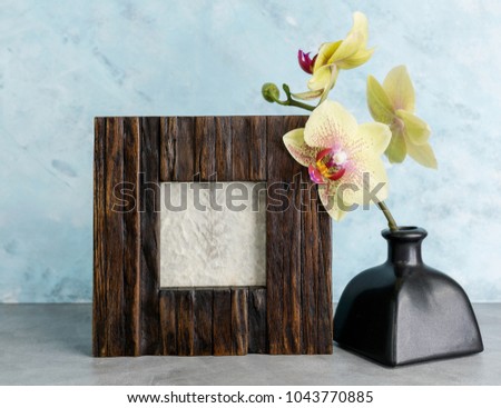 Wooden photoframe mockup with yellow orchid against  light blue wall. Interior design concept. Text space