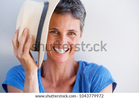 Close up portrait of smiling mature woman with hat against white wall