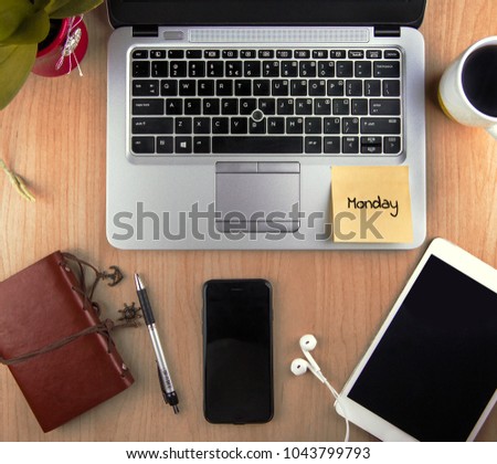 A Technology/Business Concept - high angle view of an office with a Laptop, Smart phone, Headset, Tablet, Notepad, Pen, Coffee, plant on a desk with a sticky note contain word "Monday".