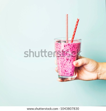 Banana currant smoothies of violet color with red straws on a blue background in the hand. Healthy food and diet concept . Background, copyspace Royalty-Free Stock Photo #1043807830