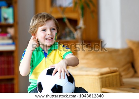 Little blond preschool kid boy with ball watching soccer football cup game on tv.