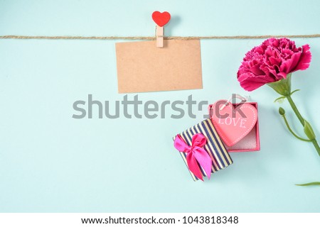 May mother's day idea, beautiful carnation with pink colour heart shape love giftbox isolated with blue green background and kraft card on a clip, topview, copyspace, closeup, flatlay, mockup