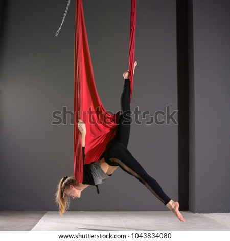 Fly yoga. Young woman practices aerial anti-gravity yoga with a hammock in fitness club on gray background.