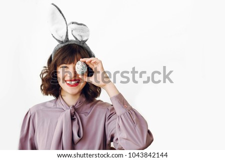 happy Easter. beautiful stylish girl in bunny ears holding colored easter egg on white background isolated. funny easter hunt concept. happy woman smiling with egg at face. fun moments