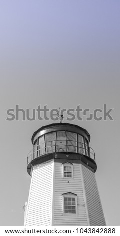 A low angle view, black and white photo of a historic nineteenth century white lighthouse in a small town in Canada.