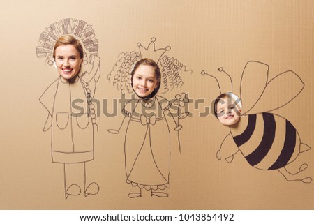 partial view of smiling mother and daughters with heads in cardboard paper with pictures