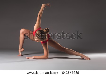 Thin young lady in red leotard doing gymnastic exercise on the floor with elegance