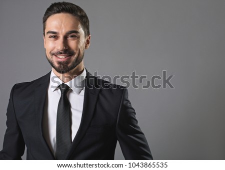 Sense of joy. Waist up portrait of bearded joyful man in business suit, he is looking at camera with felicity. Isolated on grey background and copy space in right side