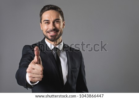 It is great. Waist up portrait of standing young smiling businessman showing ok sign. Isolated on grey background and focus on hand. Copy space in right side