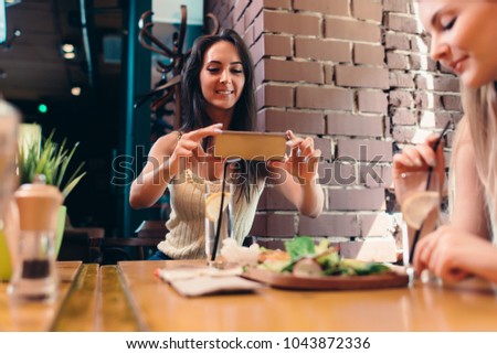 Two girlfriends having healthy lunch in cafe. Young woman taking picture of food with smartphone posting on social media