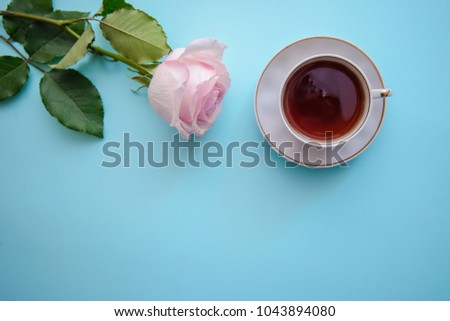 Romantic picture with a pink rose and a cup of tea on a blue background