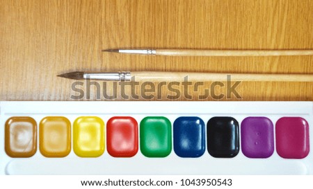 Set of watercolors aquarelle and two paint brush on wooden table. Colorful stationery for artist and school studying, design element or background wallpaper