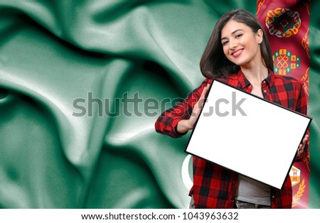 Woman holding blank board against national flag of Turmenistan