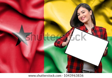Woman holding blank board against national flag of Guinea Bissau