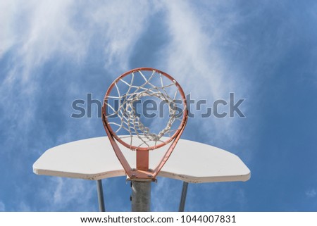Upward view a basketball hoop in public arena at community park in Irving, Texas, USA. Lookup of rim and white backboard under cloud blue sky