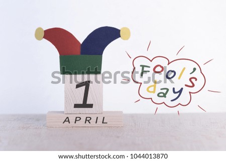 Fools' Day, date April 1 on wooden calendar and clown cap on a white background