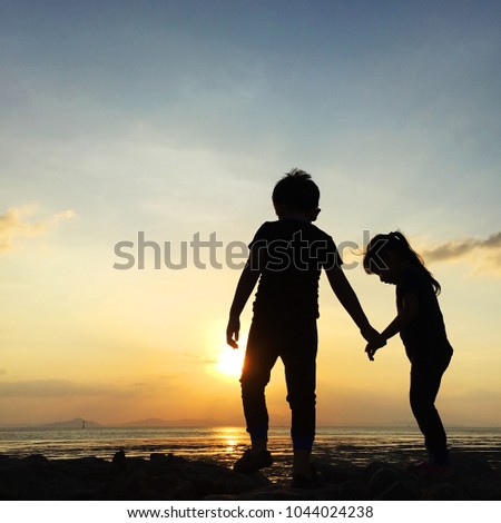 Silhouette of two sibling playing together at the beach on sunset
