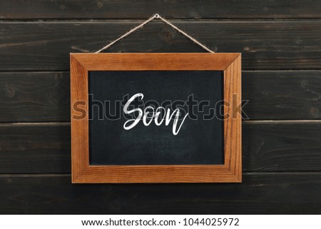 Board with lettering soon hanging on wooden wall