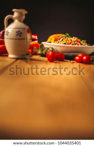 A view of a spelled dish on wooden background with some ingredients around: carrots, peppers, tomatos, parsley and oil