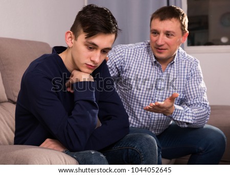 Boy is offended and father is asking for his forgiveness at the home. Royalty-Free Stock Photo #1044052645