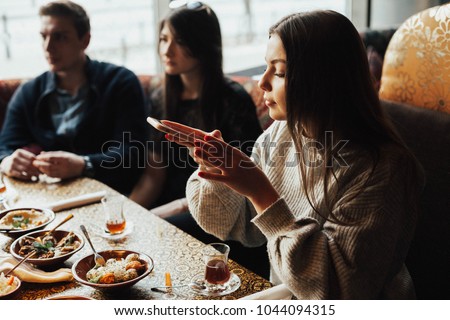 Young girl is taking pictures of food. A young company of people is smoking a hookah and communicating in an oriental restaurant. Lebanon cuisine served in restaurant.  Traditional meze lunch