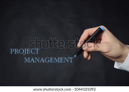 The businessman writes a blue marker inscription:PROJECT MANAGEMENT