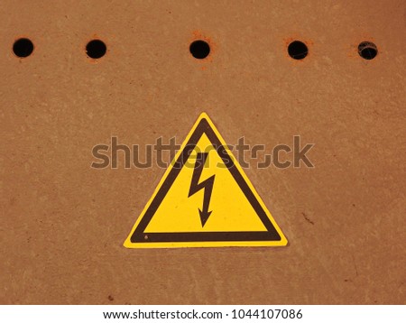 Sign of high voltage on brown metal with perforation.