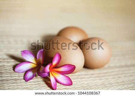 Three natural brown eggs with flowers are lieing on the straw rug