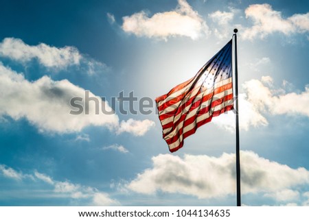 Perfect sunny day with puffy white clouds and direct sunshine into the perfect American flag illuminated back lit by sun. United States flag waving in the wind on a dramatic sky day direct sunshine