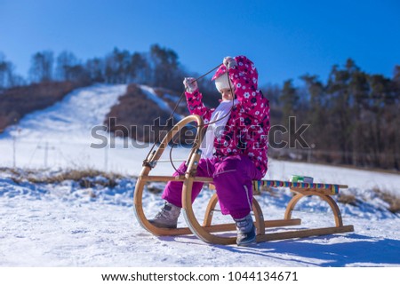 Little girl enjoying a sleigh ride. Child sledding. Children play outdoors in snow. Outdoor fun for family Christmas vacation.
