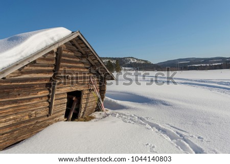 Old timbered barn with a pair of ski leaning against it and a blue sky and moutains in background, picture from  Northern Sweden.